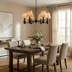In matte black, this Clérachic chandelier glows above a dark wood dining table with upholstered grey chairs.