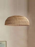 Close view of this Clérachic pendant's shallow rattan dome against a plain wall, a framed picture just visible below.