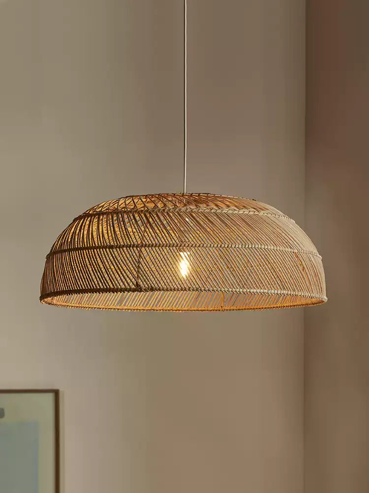 Close view of this Clérachic pendant's woven rattan dome, lit softly against a plain wall.