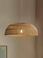 Close view of this Clérachic pendant's woven rattan dome, lit softly against a plain wall.