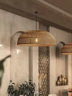 In a hallway with a stone-textured wall, this Clérachic pendant hangs beside an arched niche holding potted plants.