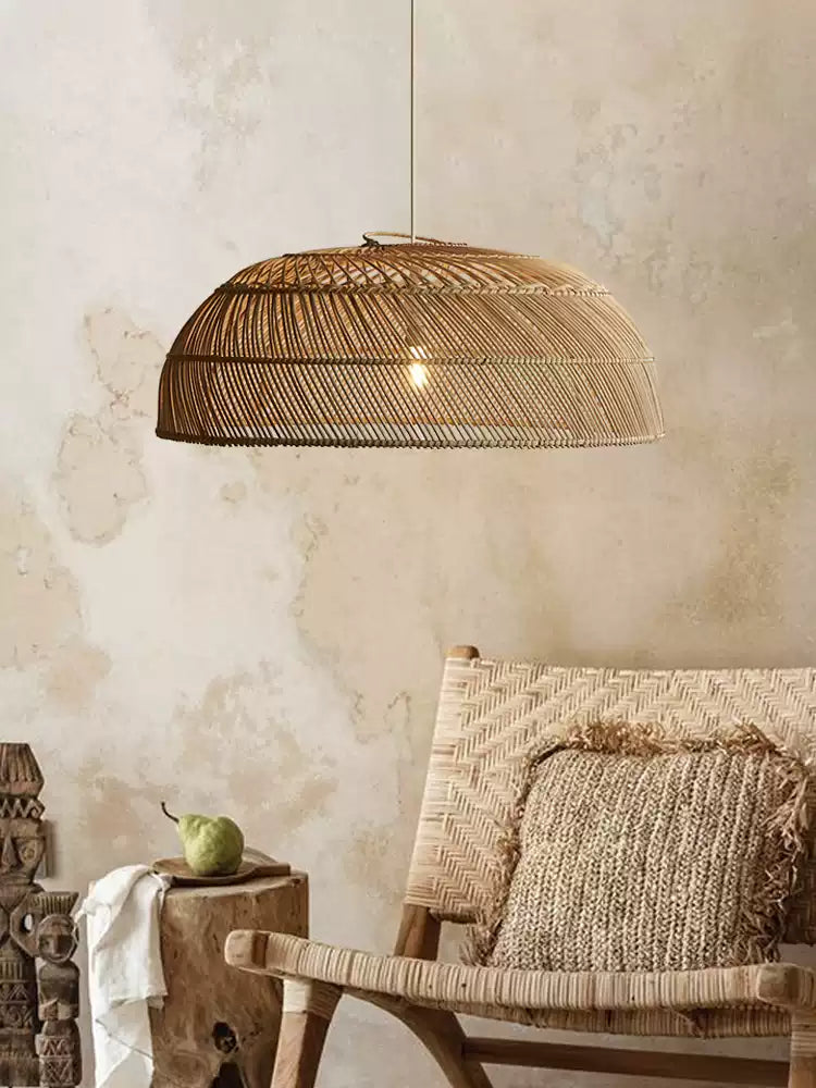 Against a textured plaster wall, this Clérachic pendant hangs near a woven wicker chair with a patterned cushion.