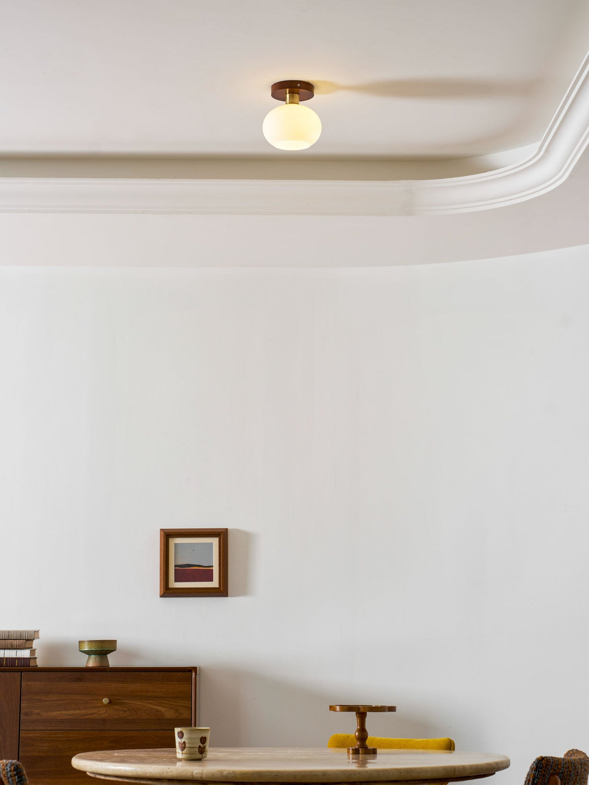A dresser and framed print sit below this Clérachic ceiling light, glowing warm along a crown-moulded ceiling.