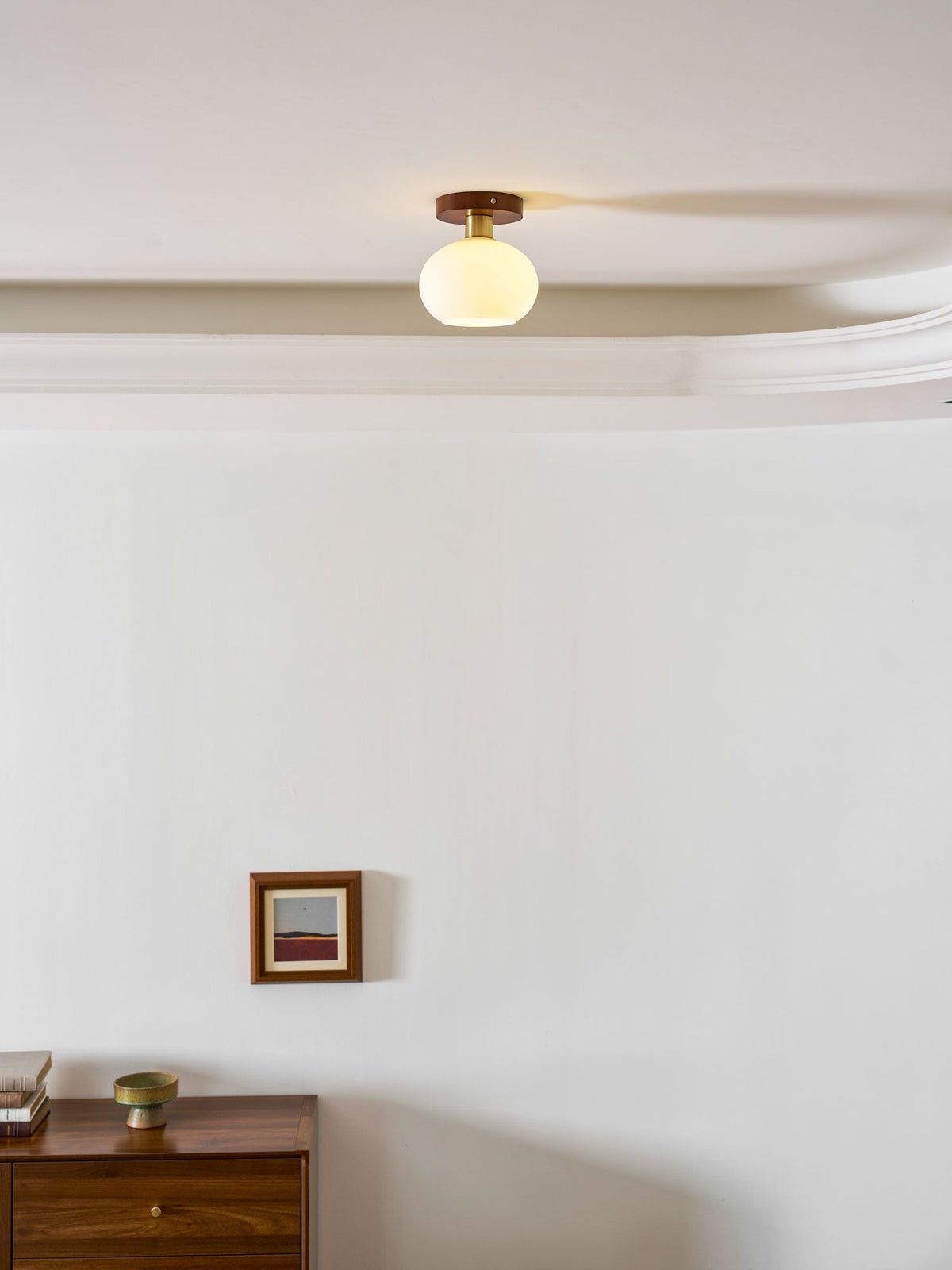 A small framed print and a wood dresser sit below this Clérachic ceiling light along a crown-moulded ceiling.