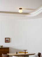 A round table set with a vase sits beneath this Clérachic ceiling light, glowing warm in a softly lit room.