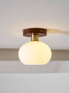 Angled close, this lit Clérachic ceiling light shows warm light glowing through its opal glass shade beneath a walnut canopy.