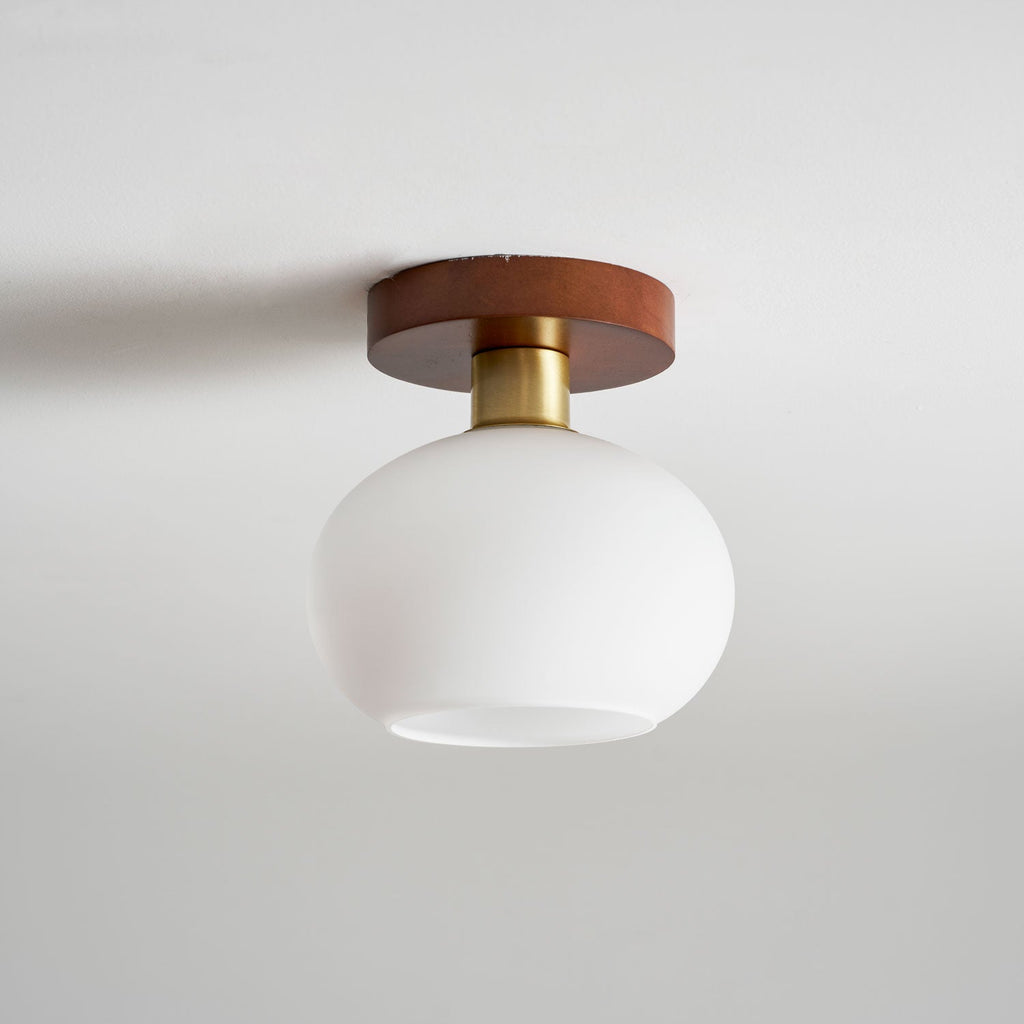 From the side, this unlit Clérachic ceiling light shows its opal glass shade curving beneath a walnut canopy.