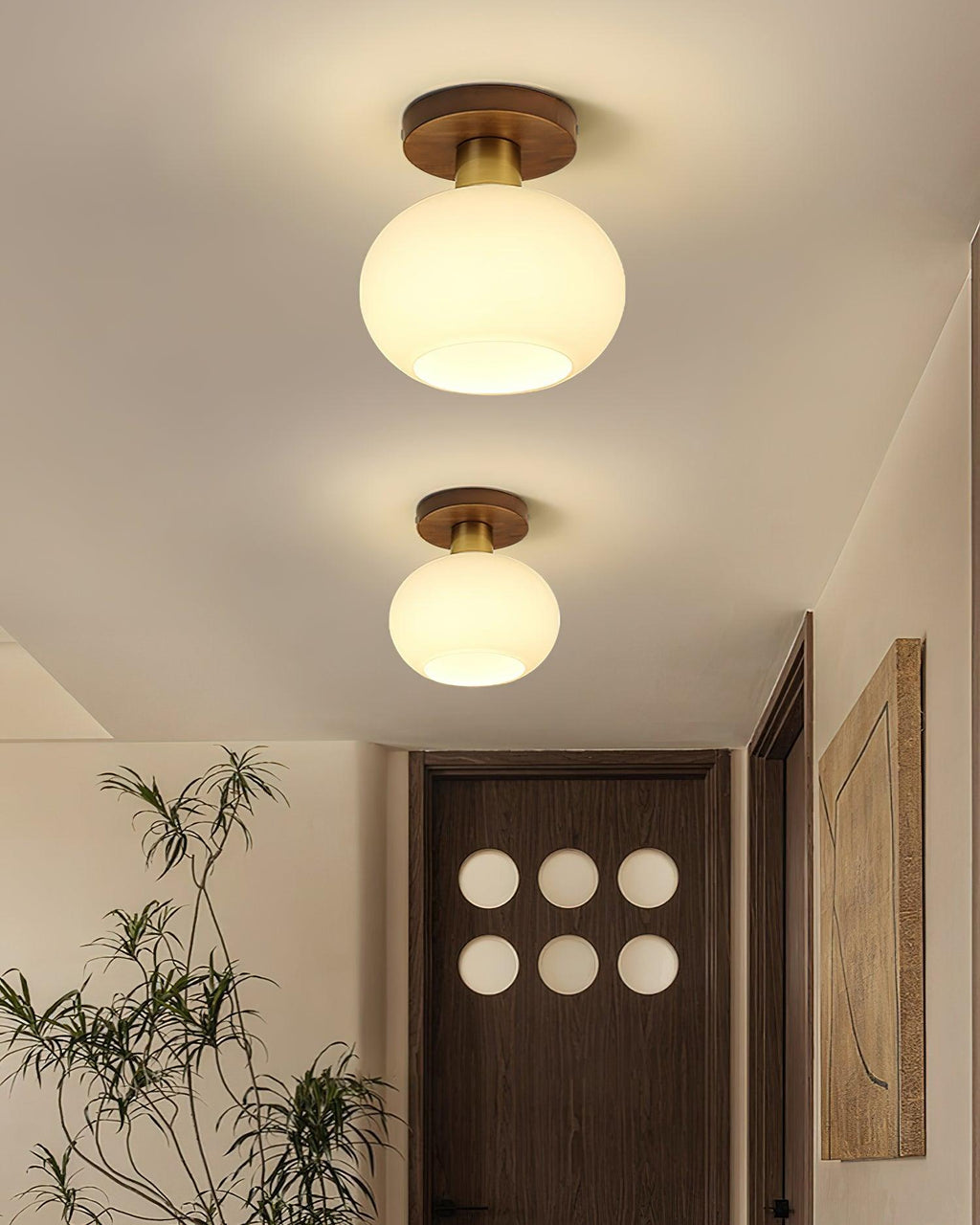 A potted plant and panelled door sit beneath two of these Clérachic ceiling lights, glowing warm in a hallway.