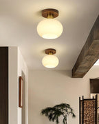 Beneath a wooden ceiling beam, two of these Clérachic ceiling lights glow warm above a dark hallway door.