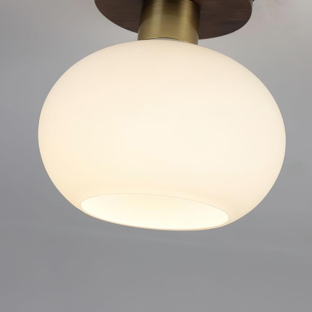Tilted at an angle, this unlit Clérachic ceiling light shows its rounded opal glass shade beneath the walnut canopy.