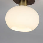 Tilted at an angle, this unlit Clérachic ceiling light shows its rounded opal glass shade beneath the walnut canopy.