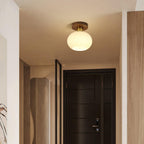 A dark wood entry door sits below this Clérachic ceiling light, glowing warm overhead.
