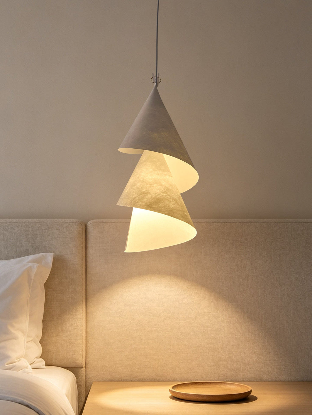 Beside a bed with an upholstered headboard, this Clérachic pendant's cones catch the lamp light nearby.