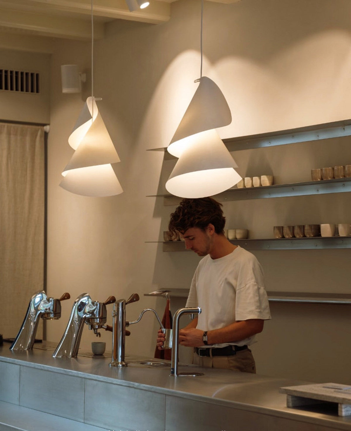 Two spiralling paper-cone pendants from this Clérachic fixture light a kitchen counter with brass taps.