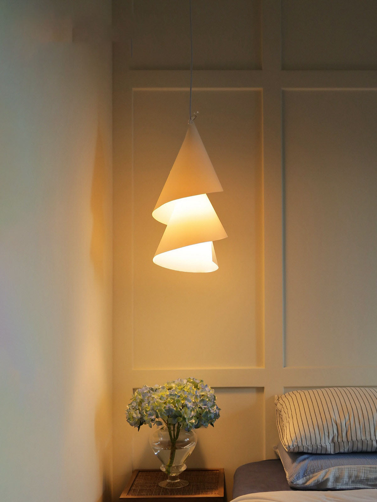Near a panelled wall and a vase of blue flowers, this Clérachic pendant lights a quiet bedroom corner.