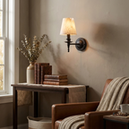 This matte black Clérachic wall sconce lights a greige wall beside a leather armchair and a wooden console table.