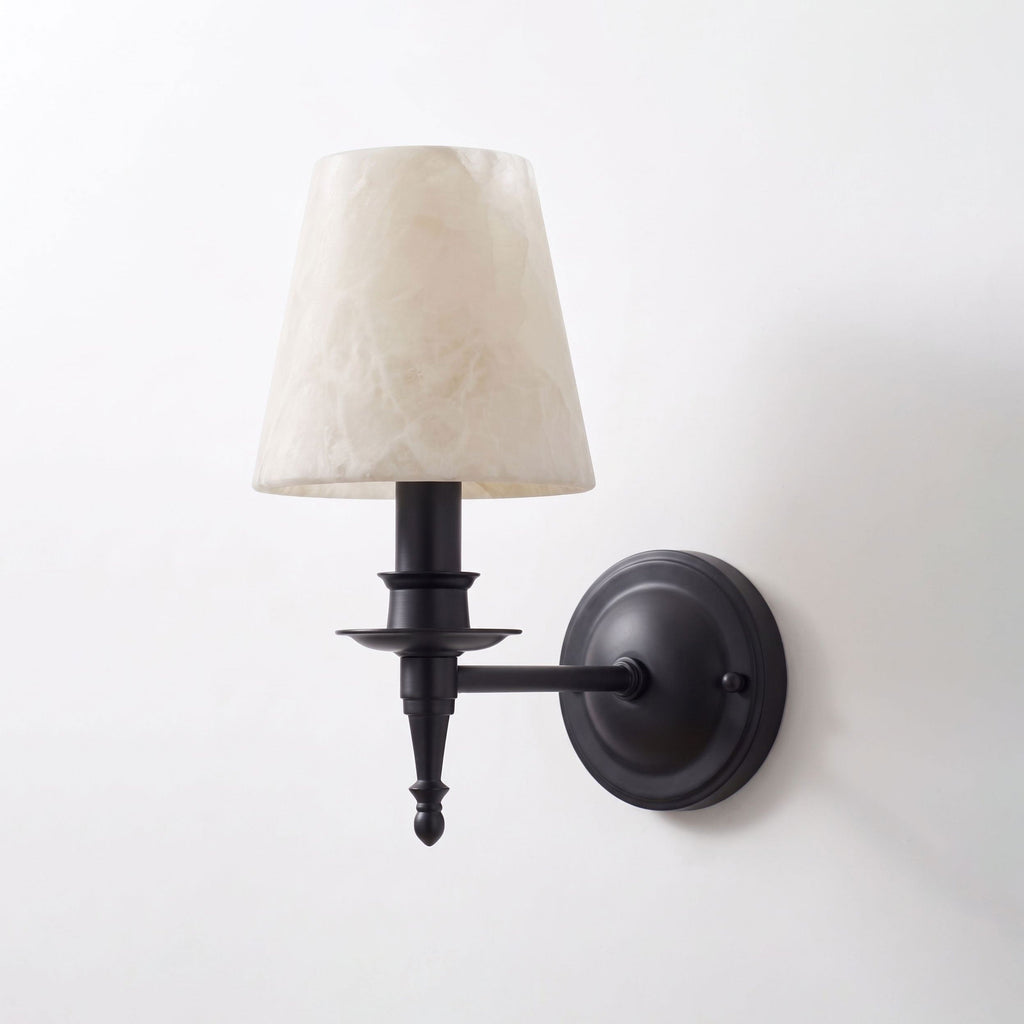 Shown unlit against white, this matte black Clérachic wall sconce reveals its candlestick column and scalloped drip pan.