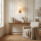 On a white panelled wall, this brushed brass Clérachic wall sconce glows above a console dressed with books and a vase.