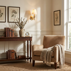 Framed botanical prints hang near this matte black Clérachic wall sconce, glowing above a console with a small clock.