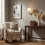 Beside a cream armchair dressed with a pillow and throw, this matte black Clérachic wall sconce glows above a console.