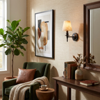 Beside a green velvet armchair, this matte black Clérachic wall sconce glows on a grasscloth-papered wall near a round mirror.
