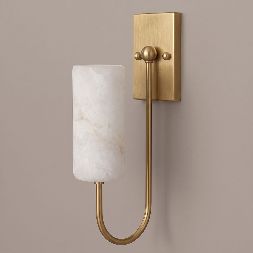 Lit on a plain taupe backdrop, this brushed brass Clérachic sconce shows its looped arm and alabaster drum shade.