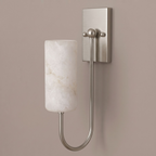 On a plain taupe backdrop, this brushed nickel Clérachic sconce glows, its cylindrical shade catching the light.