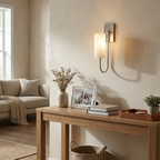 Above a console table with a framed photo and a potted plant, a nickel Clérachic sconce lights a living room wall.