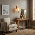 A brass Clérachic sconce glows beside an oval mirror above a console table dressed with a vase and stacked books.