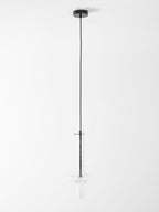 A single black-stemmed Clérachic pendant in clear glass hangs unlit on a long cord against a plain grey backdrop.