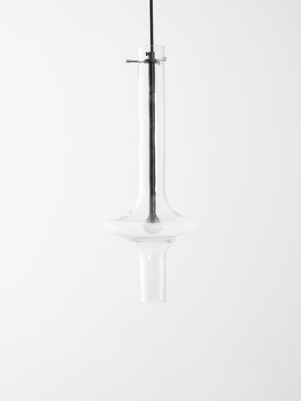 This Clérachic pendant in clear glass hangs unlit against a white backdrop, its shape mirrored in a faint reflection below.