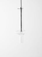 This Clérachic pendant in clear glass hangs unlit against a white backdrop, its shape mirrored in a faint reflection below.