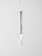 A single dark-stemmed Clérachic pendant with a gold crossbar glows in clear glass against a plain white backdrop.