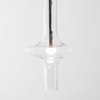 A close view shows the lit bulb inside this Clérachic pendant's flared clear glass base, with its gold crossbar visible above.