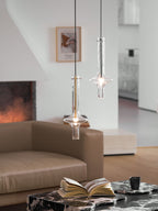 Two Clérachic pendants at different heights light a full view of a living room, with a sofa, low table, book and cup below.