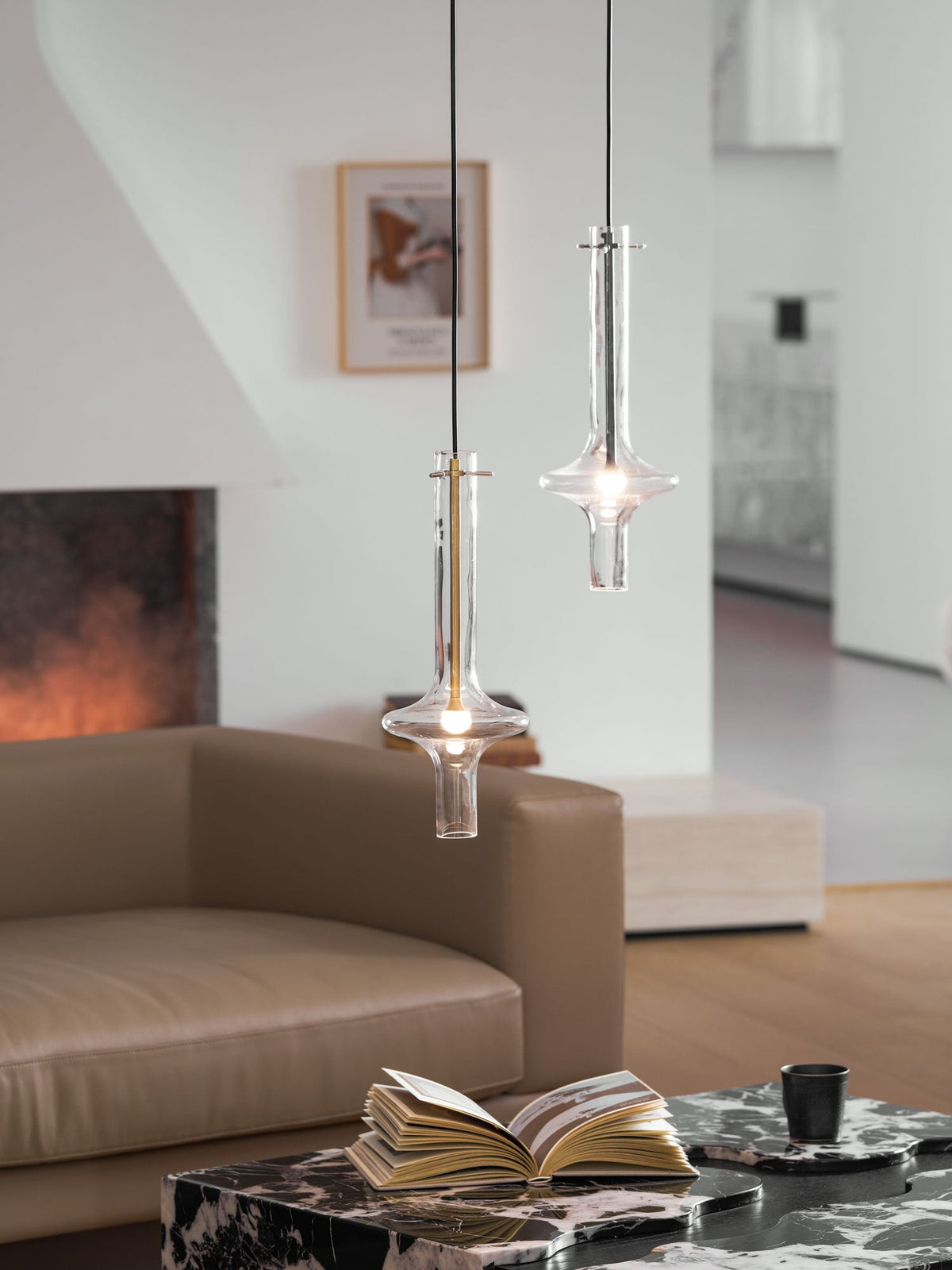 Two Clérachic pendants at different heights light a full view of a living room, with a sofa, low table, book and cup below.