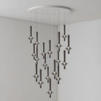 Black-stemmed Clérachic pendants cascade in an uneven spread from a round canopy, lit in the corner of a plain grey room.