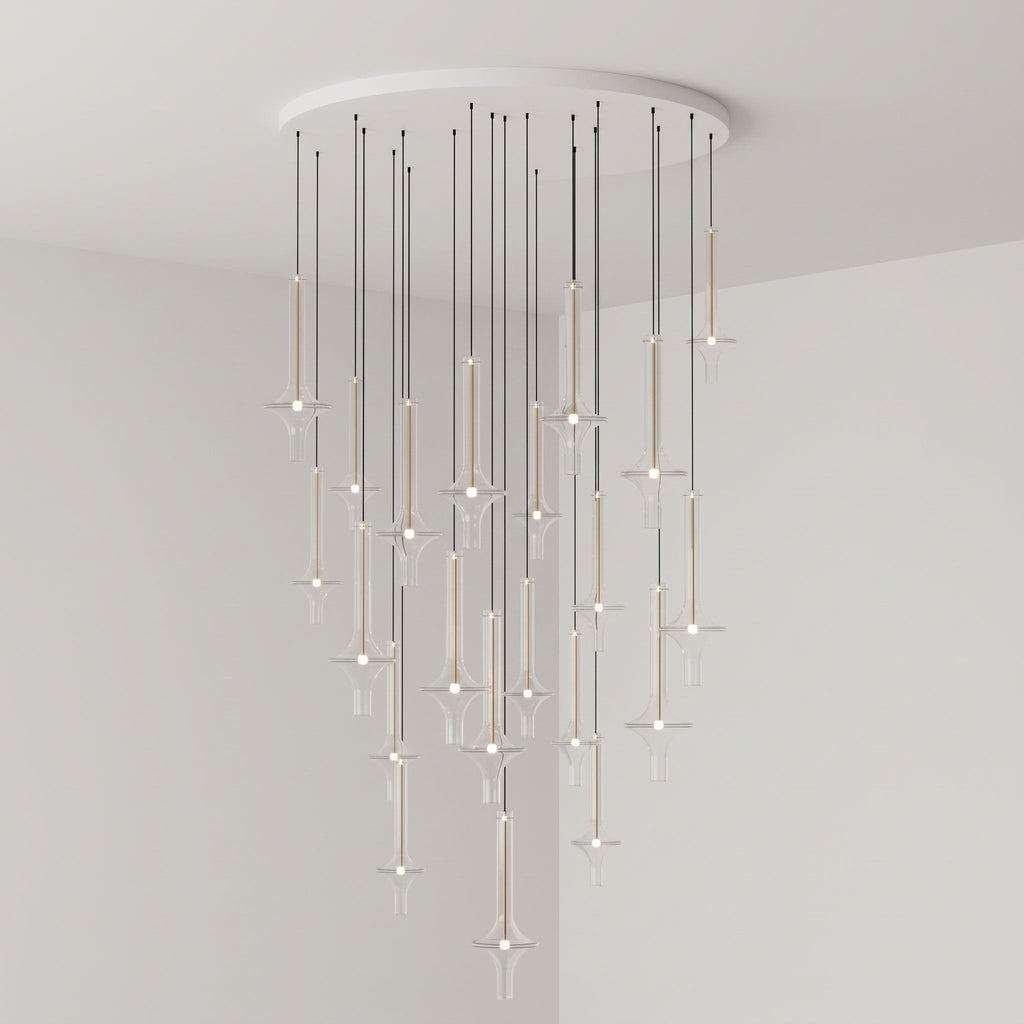 Gold-stemmed Clérachic pendants cascade unevenly from a round canopy, lit in clear glass in the corner of a grey room.