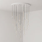 Gold-stemmed Clérachic pendants cascade unevenly from a round canopy, lit in clear glass in the corner of a grey room.
