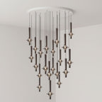 A dense cluster of black-stemmed Clérachic pendants drops from a round canopy, lit closely together in a grey corner room.