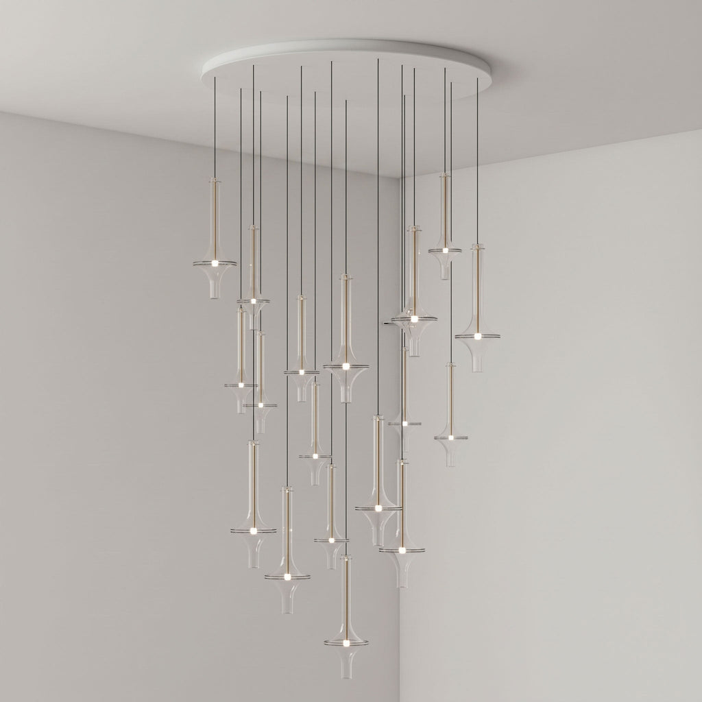 Gold-stemmed Clérachic pendants in clear glass cascade from a round canopy, lit in the corner of a plain grey room.