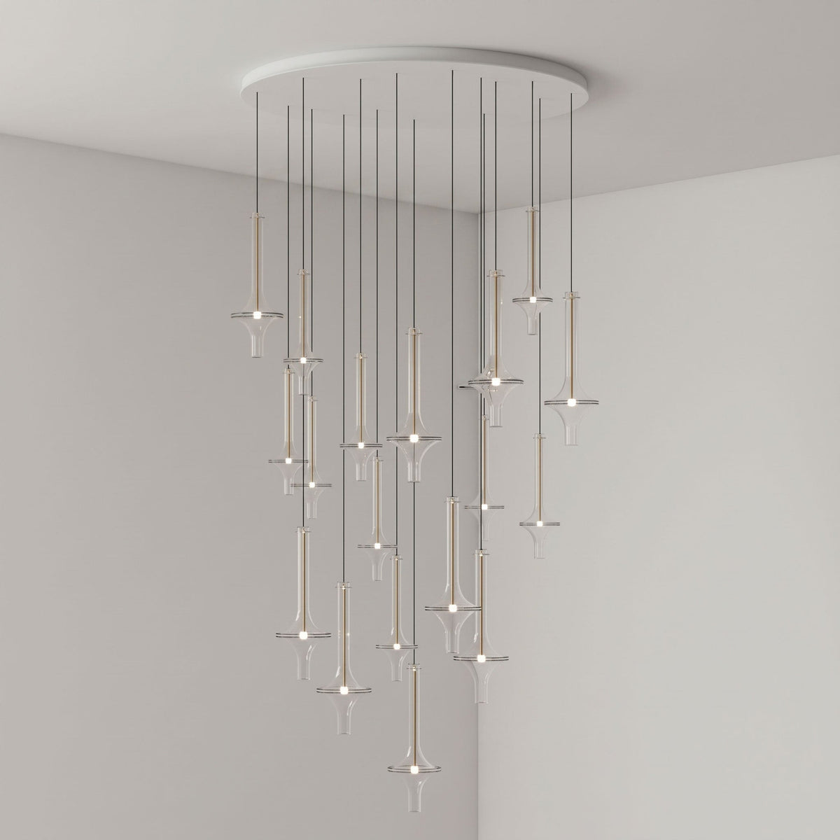 Gold-stemmed Clérachic pendants in clear glass cascade from a round canopy, lit in the corner of a plain grey room.