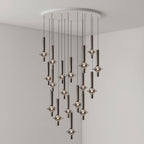 Black-stemmed Clérachic pendants cascade from a round canopy in a broad spread, lit in the corner of a grey room.