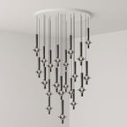 A dense cluster of lit black-stemmed Clérachic pendants drops from a round canopy in the corner of a grey room.