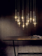 A cluster of lit Clérachic pendants hangs above a dark wood table with an open magazine, against a warm brown wall.