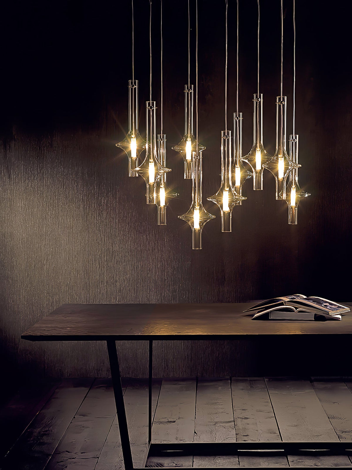 A cluster of lit Clérachic pendants hangs above a dark wood table with an open magazine, against a warm brown wall.