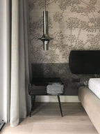 A single nickel-toned Clérachic pendant hangs beside a bed with textured floral wallpaper and a dark bedside table.