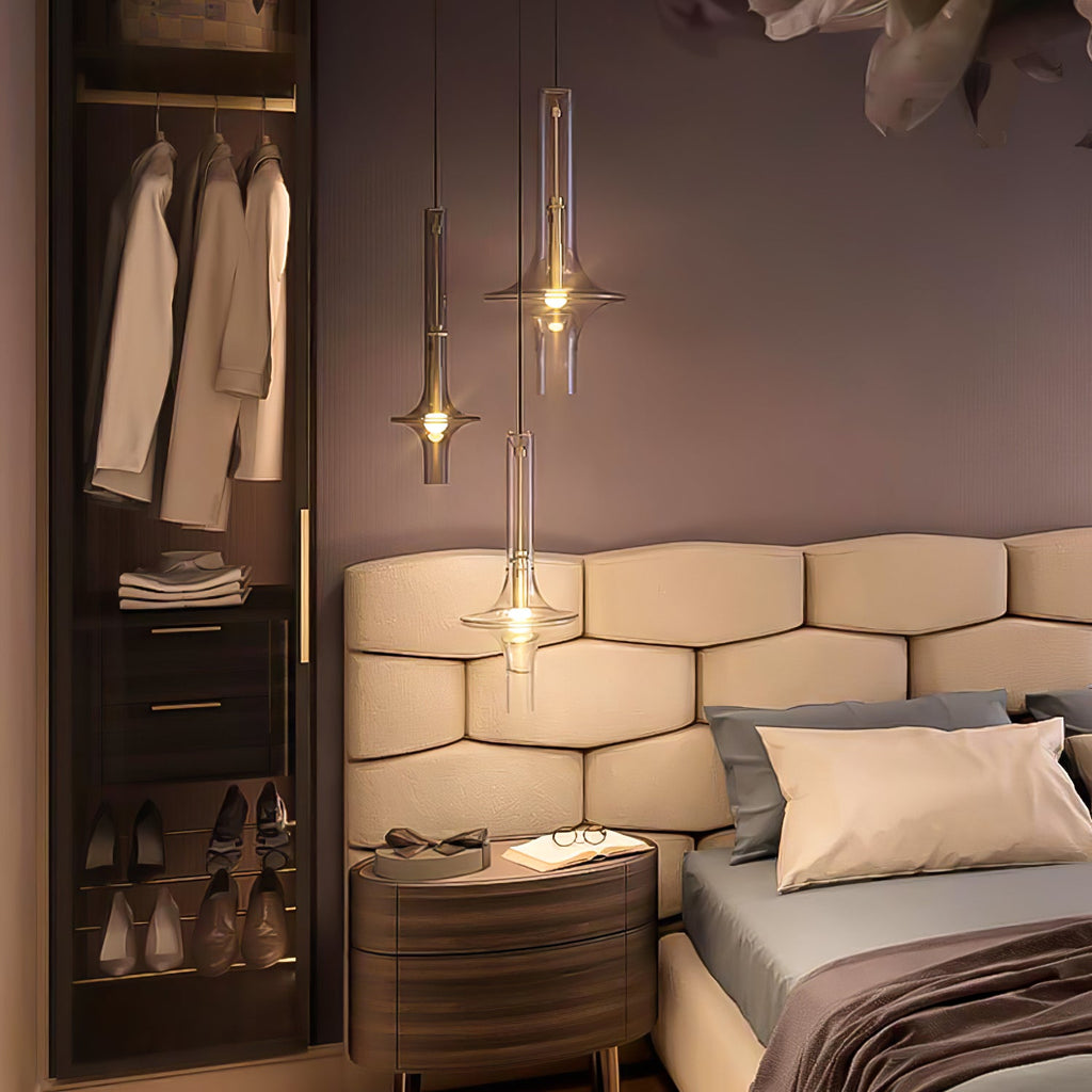 A single gold-stemmed Clérachic pendant with clear tapered glass glows beside a bed and hanging clothes in a dressing area.