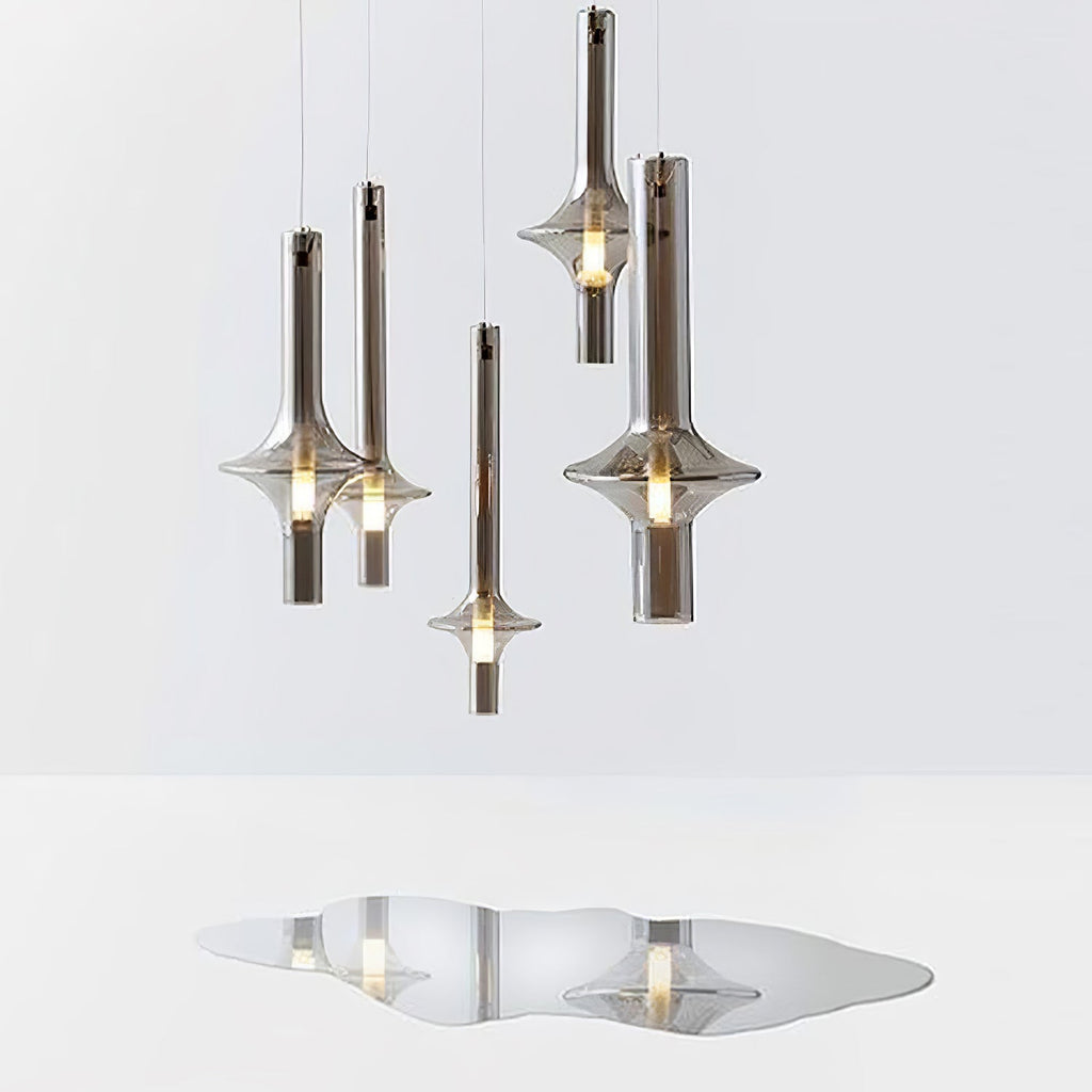 Several Clérachic pendants at staggered heights are shown on white, their forms echoed in a soft reflection on the surface below.
