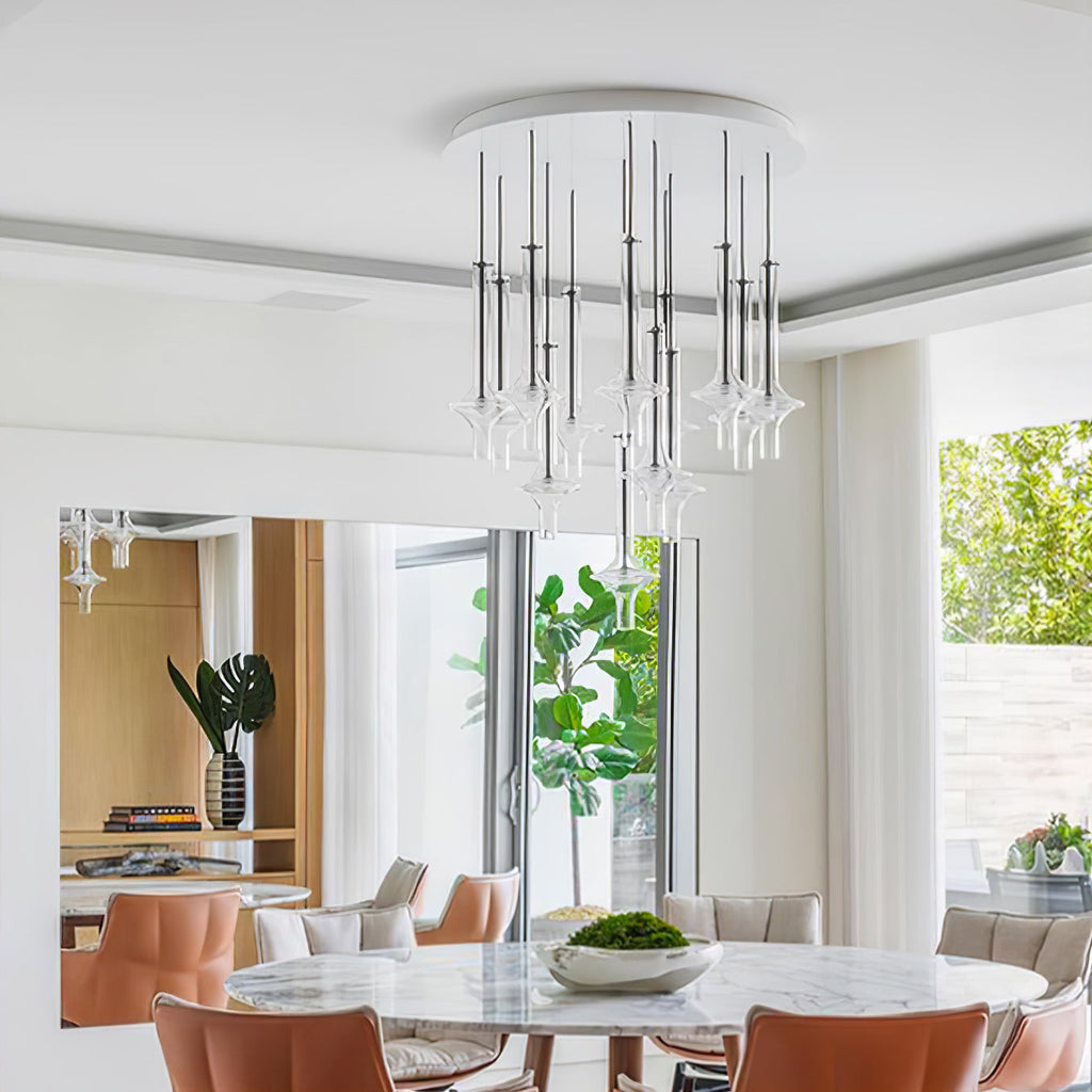 A cluster of Clérachic pendants in clear and nickel-toned glass hangs from a round ceiling plate above a dining table with tan chairs.